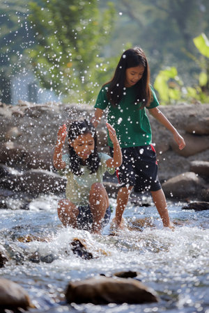 Two asian siblings playing splash water on the waterfall together with fun. Outdoor activity for children on vacation.の写真素材