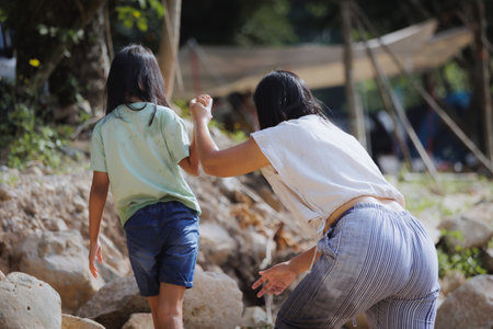 Asian mother and her daughter holding hand together and walking on the rock after play water on the river. Outdoor activity for family on vacation.の写真素材