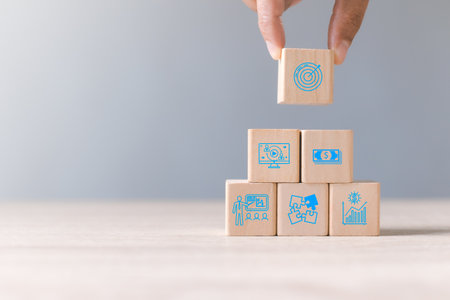 Hand is stacking wood block with icon about business strategy and action plan. Dartboard and arrow for set up business objective target. Goal and targeting the business concept. Copy space.の写真素材