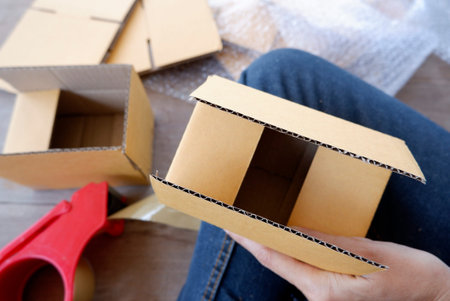 A person sits folding brown parcel boxes on a wooden floor