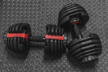 Adjustable weight dumbbell in plastic polymer material on black rubber floor.Users can choose the weight of the exercise program as needed for bodybuilding.の写真素材