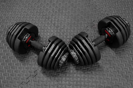 Adjustable weight dumbbell in plastic polymer material on black rubber floor.Users can choose the weight of the exercise program as needed for bodybuilding.の写真素材