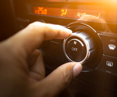 A hand is adjusting level temperature control button of air condition on dashboard in the cockpit of a car.の写真素材