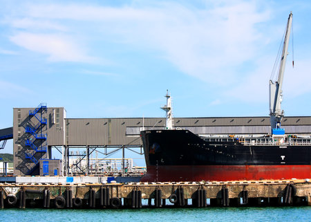 Port berth with material handling equipment and cargo vessel at anchor