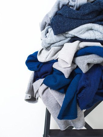 Pile of grey and blue woolen sweaters on stool over white background. Cleaning concept.の写真素材