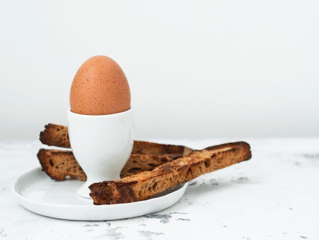 Soft-boiled egg in eggcup with crouton on white table