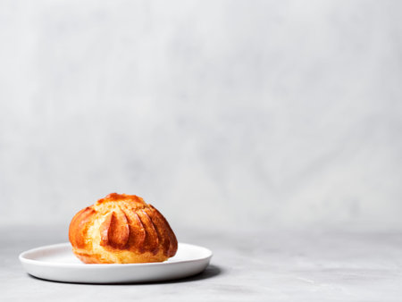 Close up of large delicious profiteroles with custard served on a white plate on a gray background.