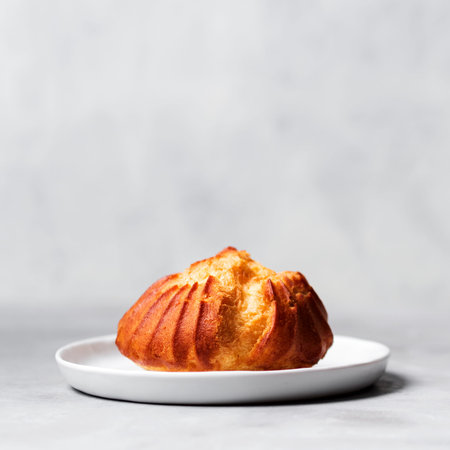 Close up of large delicious profiteroles with custard served on a white plate on a gray background.