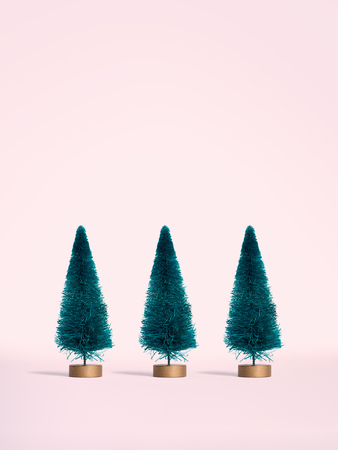 Small artificial Christmas trees on pink postel background. Minimal style. Christmas and New Year concept.の写真素材