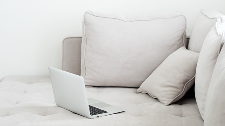 Open laptop lying on a gray sofa. Minimalistic style in a light key. Side view.の写真素材