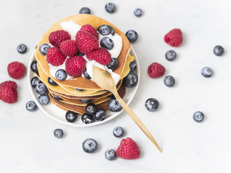 Delicious stack of pancakes close-up with fresh blueberry and raspberry on a small plate on light background.  Good idea for sweet breakfast.の写真素材