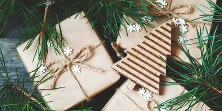 Close-up of Christmas gifts Packed in kraft paper with wooden toy among the branches of the Christmas tree. New year greeting card concept, holiday mood. Christmas or New Year background.の写真素材