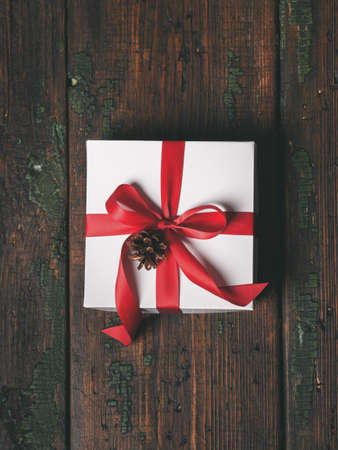 Christmas, New Year holiday background. Top view of gift white box decorated red ribbon and glitter balls over wooden table with copy space.の写真素材