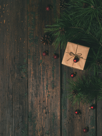 Christmas, New Year holiday background. Flat-lay of gift box decorated craft paper and red glitter balls, fir branches and pine cones over wooden tableの写真素材