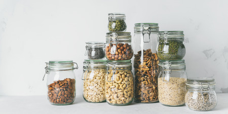 Glass jars with Superfoods, almonds, cashews, peanuts, hazelnuts, walnuts and Chia seeds, mung beans, quinoa, sunflower seeds on light background with copy space. Balanced diet.の写真素材