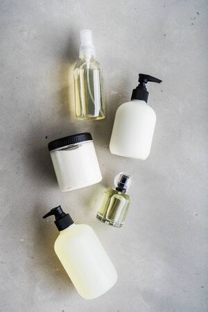 Cosmetic set of blank label bottles for mockup packaging of skincare product cream, serum, oil, shampoo, conditioner, perfume on grey background with green leaves. Natural beauty product concept.の写真素材