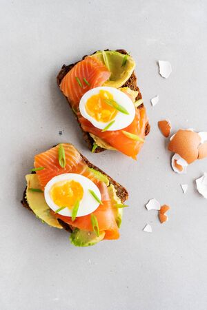 Healthy open sandwiches on multigrain wholegrain  toast with avocado, salmon, eggs, herbs, sunflower seeds over white plate on concrete background with copy space. Healthy protein food.の写真素材