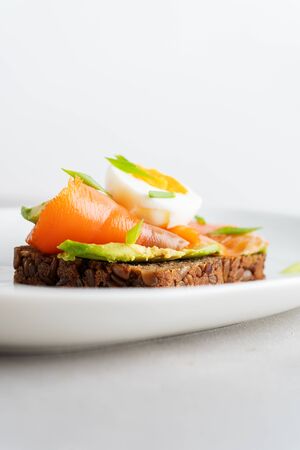Healthy open sandwiches on multigrain wholegrain  toast with avocado, salmon, eggs, herbs, sunflower seeds over white plate on concrete background with copy space. Healthy protein food.の写真素材