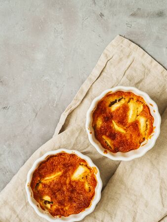 Flat lay of prepared apple cakes, tarts, puddings in a porcelain baking dish on a gray concrete background with a linen napkin and space for the recipe textの写真素材