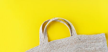 Eco friendly wicker Straw bag over yellow background with space for text, top view, wide composition. Summer vacation fashion, holiday concept. Beach accessories.の写真素材