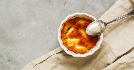 Flat lay of prepared apple cakes, tarts, puddings in a porcelain baking dish on a gray concrete background with a linen napkin and space for the recipe textの写真素材