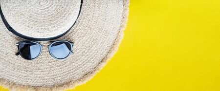 Eco friendly wicker straw hat with sunglasses over yellow background with space for text, top view, wide composition. Summer vacation fashion, holiday concept. Beach accessories. Long banner.の写真素材