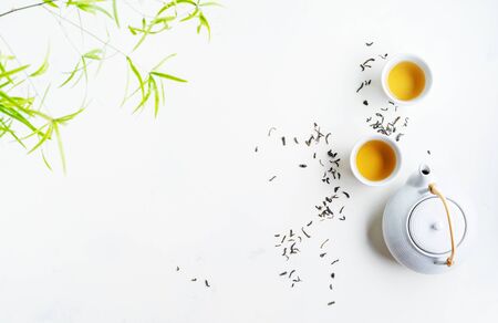 Asian tea concept, two white cups of tea and teapot surrounded with dry green tea  leaves , space for a text on white background. Brewing and Drinking tea.の写真素材