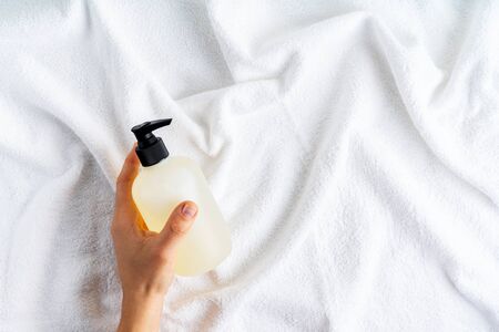 Female hand holding a bottle with organic body care cosmetic product on white fluffy towels background with space for text.の写真素材
