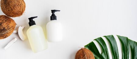 Close up of two bottles for organic body care cosmetic products on green monstera leaves, coconuts over white textile background. SPA branding mock-up, place your design of natural skincare concept.の写真素材