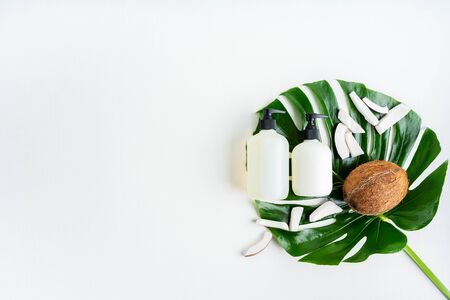 Close up of two bottles for organic body care cosmetic products on green monstera leaves, coconuts over white textile background. SPA branding mock-up, place your design of natural skincare concept.の写真素材