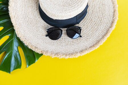 Straw hat, eco friendly wicker bag, sunglasses, monstera branches over yellow background with space for text, top view, wide composition. Summer vacation fashion, holiday concept. Beach accessories.の写真素材