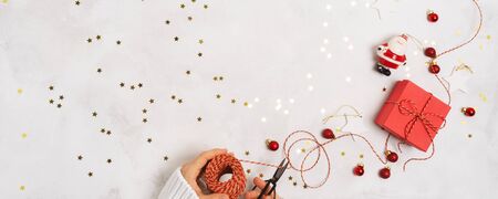 Women's hands in a sweater pack a gift box for the New year. Creative Christmas layout on white background with confetti and space for text.の写真素材