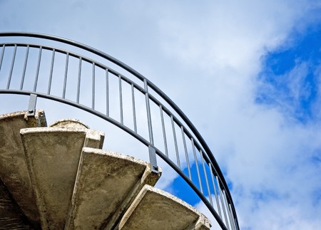 Spiral staircase seen from below against blue cloudy skyの写真素材