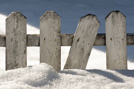 Old wooden fence in a snow drift on a sunny winter dayの写真素材