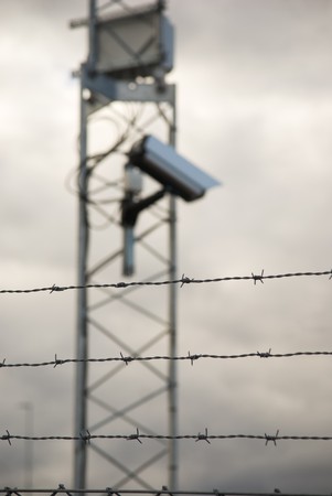Defocused surveillance camera behind barbed wire. Focus on the wireの写真素材