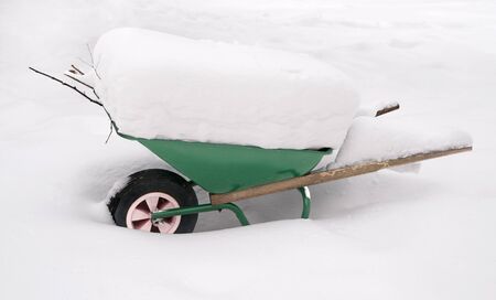 Green wheelbarrow covered in deep snowの写真素材