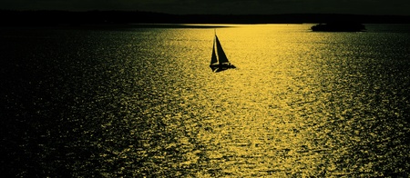 Sailing boat at sunset reflected in the waterの写真素材