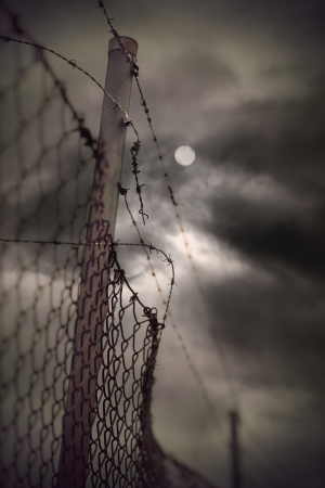 Rusty barbed wire and chain link fence with vintage look on moody evening sky with moonの写真素材