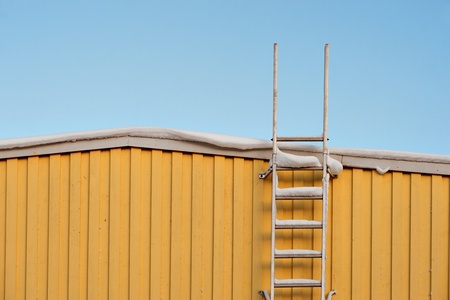 Metal ladder on yellow wooden wall in winterの写真素材