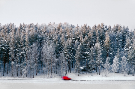 Red van in blurred motion on rural winter road with forest in backgroundの写真素材