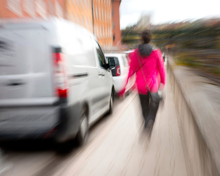 Woman in blurred motion dressed in red walking along sidewalk in busty sity streetの写真素材