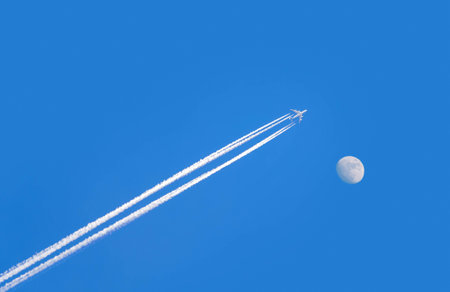 jet airplane with trail of fuel on blue sky and big moonの写真素材