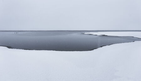 Sparse winter landscape with snow and ice on lake as well as open waterの写真素材