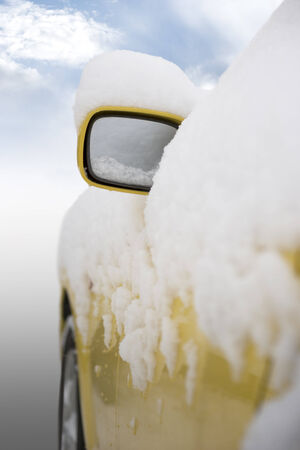 Yellow car with cap of snow on external rear mirrorの写真素材
