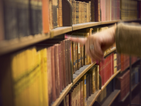 Library or book store with rows of old antique books, and a hand of a woman reaching for a bookの写真素材