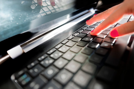 Back lit fingers of person typing on keyboard of laptop