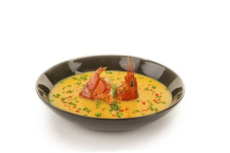 Black bowl with yellow seafood soup and lobster swiming in the middleの写真素材