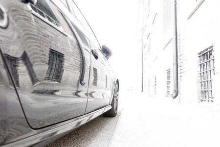 brick wall of old building with barred windows in street reflected in side of parked carの写真素材