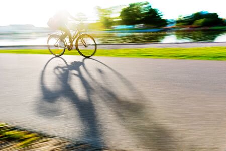 Person cycling along river in bright sunshine, casting long shadow on cycling pathの写真素材