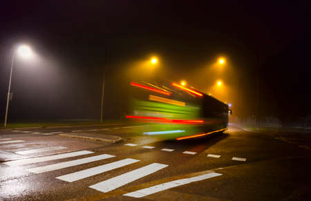 Blurred motion of green bus in dark foggy autumn eveningの写真素材